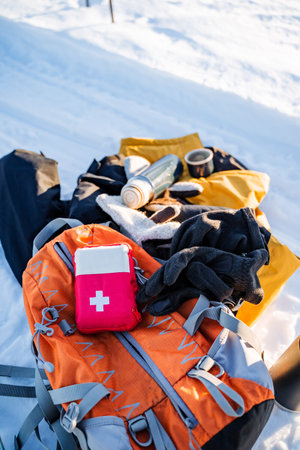 An electric blue first aid kit is placed on an orange backpack amidst the snowy landscape,...