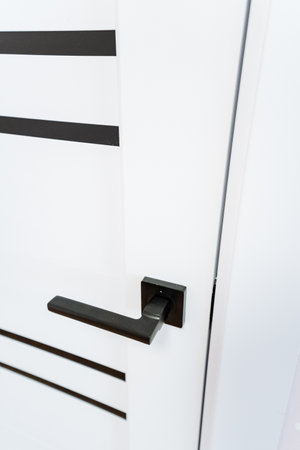 A closeup of a black rectangular door handle on a white automotive exterior, parallel to the wood grain texture of the door. The design features a sleek rim and grille on the hoodの写真素材