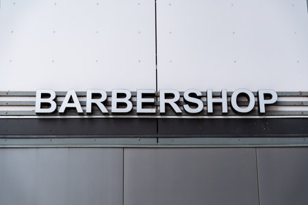 A rectangular gray metal sign with bold font hangs on the facade of the building, serving as the barbershops exterior automotive fixtureの写真素材