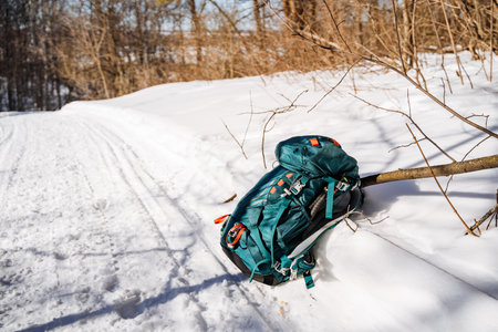 A backpack lies in the freezing snow near a tree branch, contrasting with the electric blue of the...