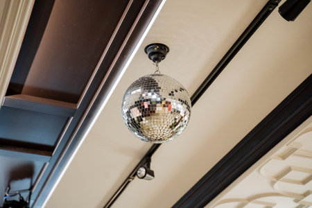 A disco ball made of glass and metal is suspended from the hardwood ceiling of a room, reflecting...