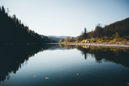 A picturesque natural landscape with a tranquil lake surrounded by trees on the bank, under a cloudy...