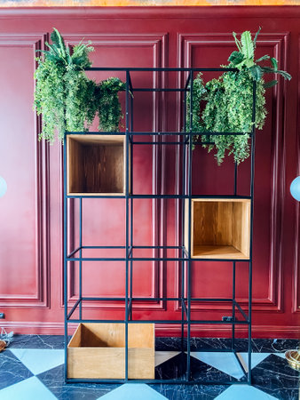 A rectangular wood shelf with plants sits in front of a red building facade, adding shades of green against the yellow wallの写真素材