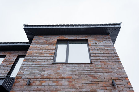 A structure made of bricks featuring two windows and a balcony. The facade showcases the sturdy brickwork against the sky backdrop. Built with composite material and wood fixturesの写真素材