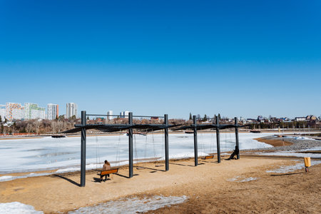 A person is relaxing on a bench in a park by a frozen lake, surrounded by a stunning natural landscape of water, sky, and cloudsの写真素材