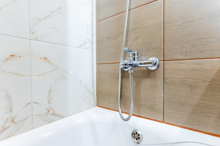 A plumbing fixture, the shower head, is mounted on the wall above a bathtub in the bathroom. It is connected to the propertys plumbing system to provide a steady flow of water for bathingの写真素材