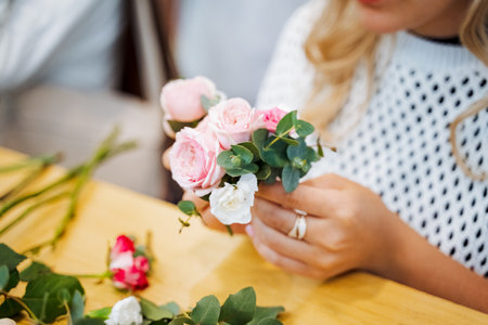 A woman sits at a table, her fingers delicately arranging a bouquet of roses. She looks happy,...