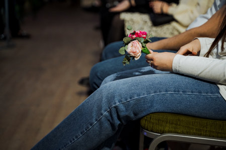 A group of individuals in denim jeans are sitting comfortably on chairs with electric blue flowers in their hands, the grass flooring adding to the leisurely atmosphereの写真素材