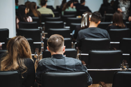 An audience is comfortably seated in chairs inside a building, sharing the room for a public speaking event. The crowd listens attentivelyの写真素材