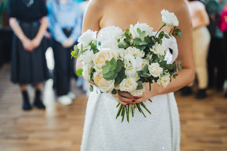 The bride looks happy in her white wedding gown, holding a bouquet of white flowers. Her gesture shows the beauty of flower arranging and elegance in formal wearの写真素材