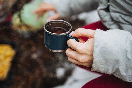 A small cup of tea in the hand of a woman on the background of the forest, a hiker on a hike holds a cup of hot drink in his hands, camping in nature. High quality photoの写真素材