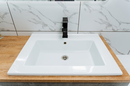 The bathroom sink features a black faucet mounted on a wooden counter top made of composite...
