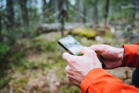 A person is holding a mobile device while surrounded by the natural landscape of the woods, filled with plants, trees, grass, and groundcoverの写真素材