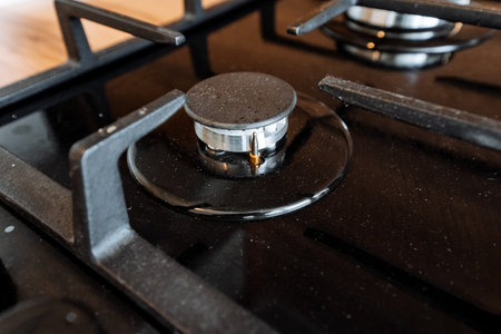 A detailed shot of a gas burner on a stove, surrounded by tableware and kitchen utensils, juxtaposed against a backdrop of hardwood and metal elementsの写真素材