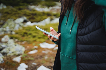 A woman is standing in a grassy field, holding a cell phone in a sleeve made of electric blue wood. Surrounded by nature and leisure activitiesの写真素材