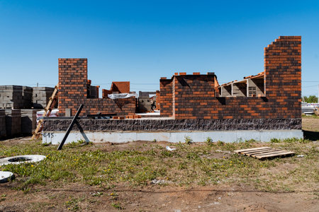 In the image, a new residential building is seen under construction with partially built brick walls and foundational work. A clear blue sky and construction materials are visible around the siteの写真素材