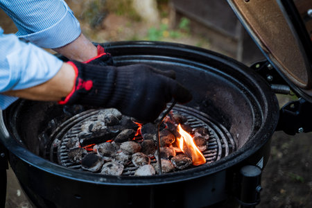 Ensuring safety, a person wears gloves to safely ignite a fire on a charcoal grill for an outdoor BBQ, enhancing the culinary experience. Enjoy the flavors of outdoor cooking with precautionの写真素材