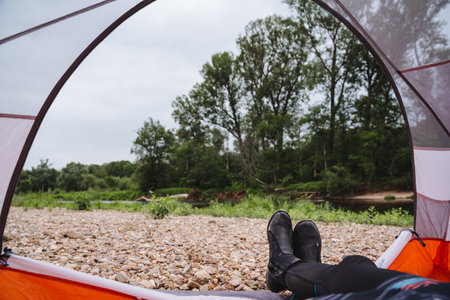 Relax and unwind on a tranquil camping trip by the riverside with a view of lush greenery from inside a cozy tent. Perfect escape into nature for outdoor enthusiasts and adventure seekers.の写真素材