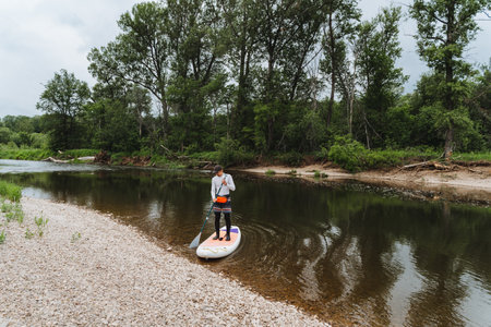 A paddleboarder peacefully blending into nature on a tranquil day, surrounded by greenery and calm...