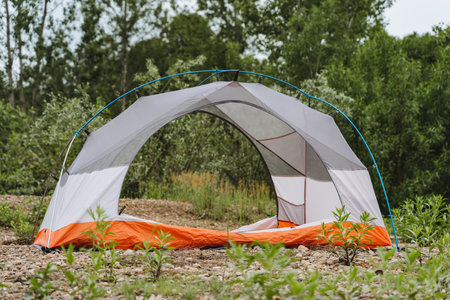 Immerse yourself in the tranquil setting of nature while setting up a camping tent. This serene image features a partially pitched tent surrounded by lush greenery, ideal for outdoor adventuresの写真素材