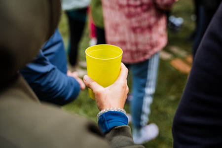 A close-up image of an individual holding a bright yellow cup, surrounded by a group of people at an...