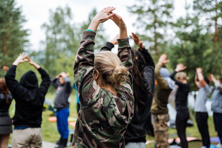 A group of people in casual clothes are bonding and promoting teamwork through outdoor stretching and warmup exercises in a serene forest. They are having fun and engaging in a healthy activityの写真素材