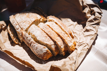 Freshly baked sourdough bread, sliced and presented on brown paper in natural lighting. Perfect for...
