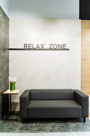 A contemporary 'Relax Zone' featuring a sleek gray sofa and a minimalist side table with a flower arrangement. The area is designed for comfort and modern aesthetics, ideal for unwinding.の写真素材
