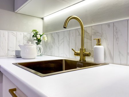 This stylish kitchen features a luxurious gold faucet, marble backsplash, and sleek white countertop, showcasing modern design and serving as inspiration for contemporary interiorsの写真素材