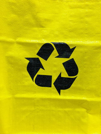 This vibrant yellow bag vividly showcases a bold black recycling symbol, perfectly highlighting its...