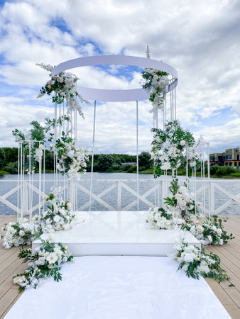 A beautifully adorned wedding arch, draped in elegant white flowers, is set on a picturesque dock that overlooks a serene lake, creating a stunning backdrop for the special occasionの写真素材