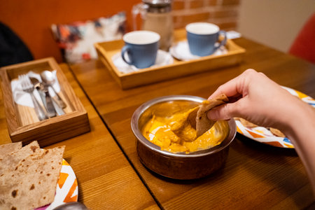 A person skillfully dips a perfectly toasted piece of bread into a bowl of mouthwatering food,...