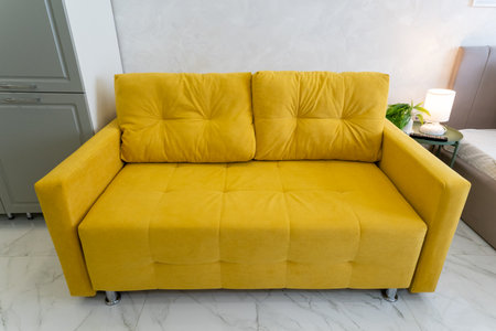 In a cozy living room, there is a bright yellow couch placed beside a comfortable bed, creating a...