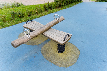 A sturdy wooden seesaw is positioned on a bright blue surface in a beautiful park that invites...