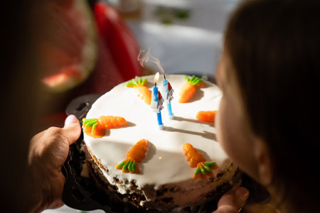 A person is gently blowing out a single lit candle that is perched on top of a delicious carrot cake during a special occasion celebrationの写真素材