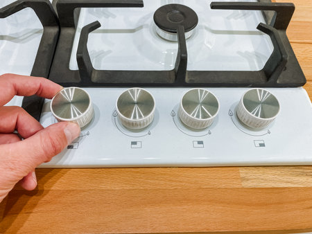 A person is focused on carefully adjusting the knobs on a gas stove in the kitchen to ensure that...