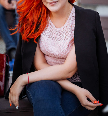 A fashionable and confident young woman with strikingly vibrant red hair sits casually in an elegant ensemble, beautifully showing her stylish look and playful personalityの写真素材