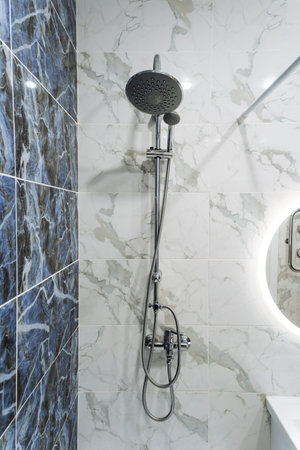 A shower head is securely mounted and hanging on a wall in a bathroom, right next to a mirror that...