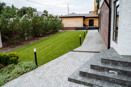 This stunningly beautifully landscaped backyard features a charming paved pathway accompanied by a vibrant green lawn filled with lifeの写真素材