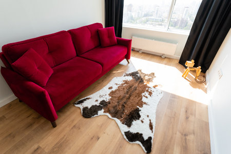 A vibrant red velvet sofa with a distinctive cowhide rug enhances the modern aesthetic of this bright living room with large floortoceiling windows for ample daylightの写真素材