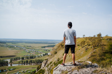 A man is standing proudly on top of a magnificent mountain, gazing out over a beautiful valley that...