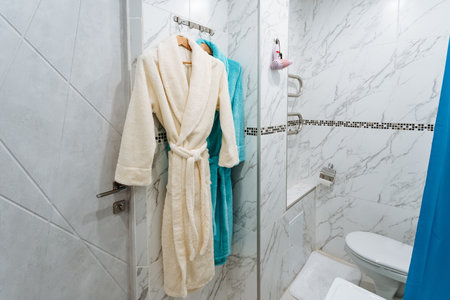 In a cozy bathroom, two plush bathrobes hang on hooks by the toilet, adding comfort and style for a relaxing experience after a refreshing bath or invigorating shower, creating a perfect retreatの写真素材