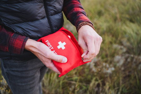A person stands in a stunning outdoor nature scene, proudly holding a bright red first aid kit in...