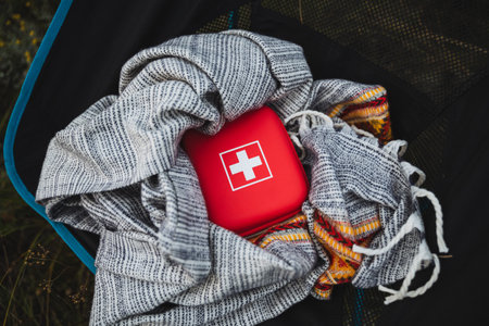 A vibrant red first aid kit is securely nestled in a cozy blanket, ideal for camping or outdoor activities, emphasizing the importance of safety and preparednessの写真素材