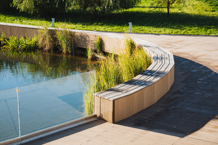Nestled beside a serene lake, a sturdy wooden bench situated in a peaceful park provides visitors...