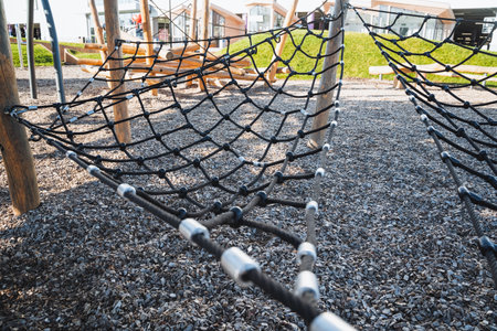 In a vibrant playground, a hammock is gently lying on the soft ground, inviting children to relax...