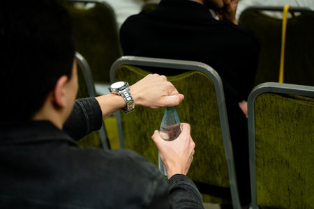 A man is seated in a chair while he is holding a bottle of water in his hand, taking a moment to...