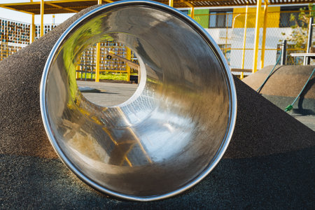 In a playground, there is a metal tube that features a noticeable hole right in the center of it, providing a unique play structure for children to explore and enjoy their time outsideの写真素材