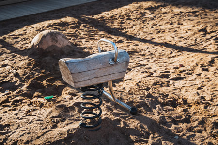 A beautifully crafted wooden rocking horse is resting serenely in the soft sand of a sunny playground, inviting children to come and play all day long in this joyful outdoor spaceの写真素材