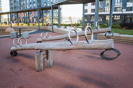 In the park, there stands a charming wooden seesaw, perfect for children to enjoy, with an interesting building visible in the background, enhancing the urban playground atmosphereの写真素材